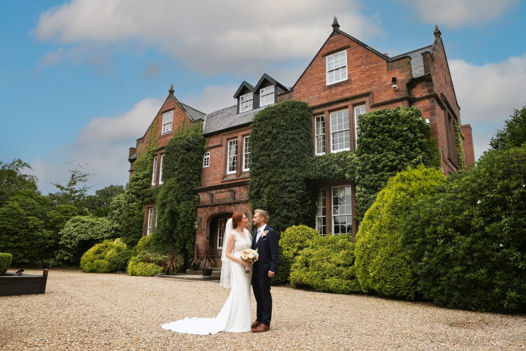 Bride and groom posing together in front of the elegant, historic architecture of Nunsmere Hall.