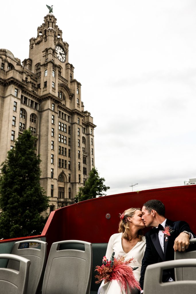 Bride and groom on a double decker bus in from of the Liver Buildings in Liverpool.