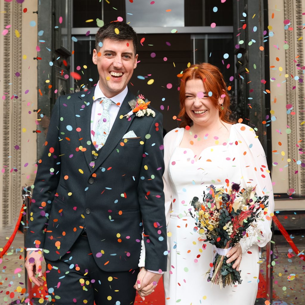 Joyful confetti moment for the newly wedded couple on the steps of the iconic St. George's Hall, Liverpool. Brightly coloured confetti showers the bride and groom against the neoclassical architecture of the Grade I listed building.