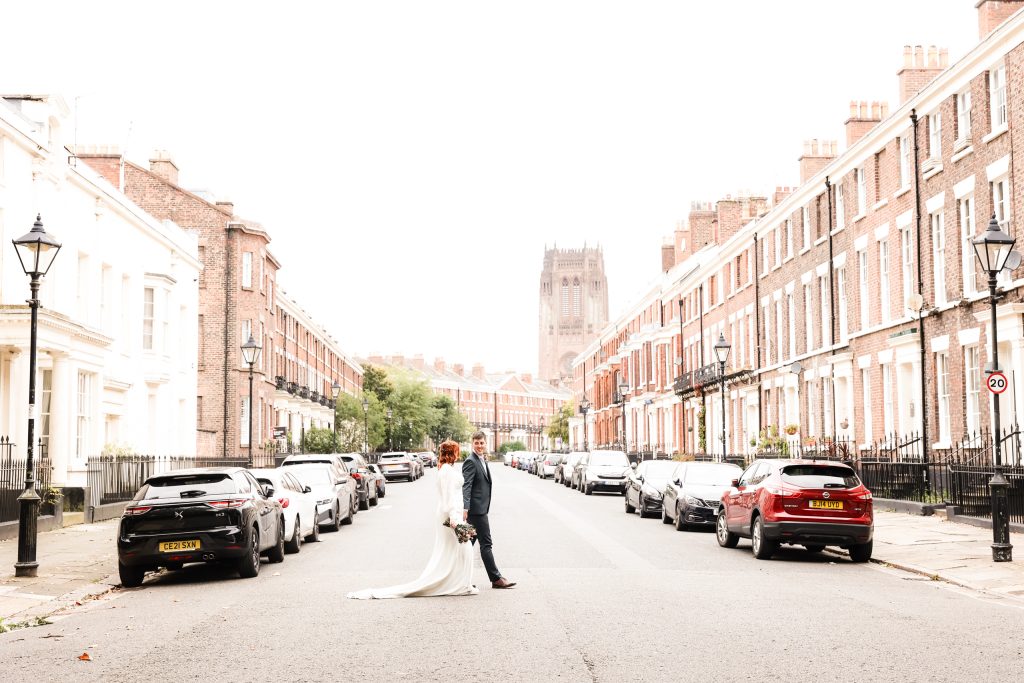 Romantic photo of a stylish bride and groom crossing a road in the historic Liverpool Georgian Quarter, with elegant terraced houses and cobbled streets in the background.