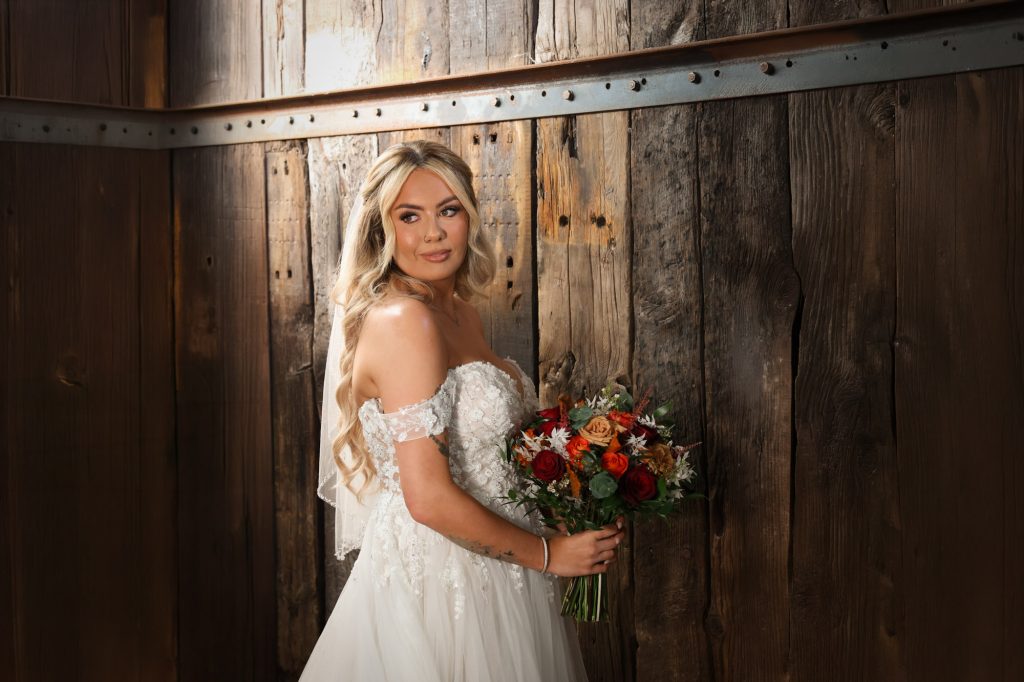 Beautiful bride holding a floral bouquet while posing against rustic wooden barn walls at Owen House Wedding Barn