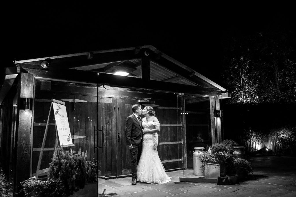 A dramatic, high-contrast black and white photograph highlighting the stunning timber roof structure of the ceremony barn at Owen House Wedding Barn