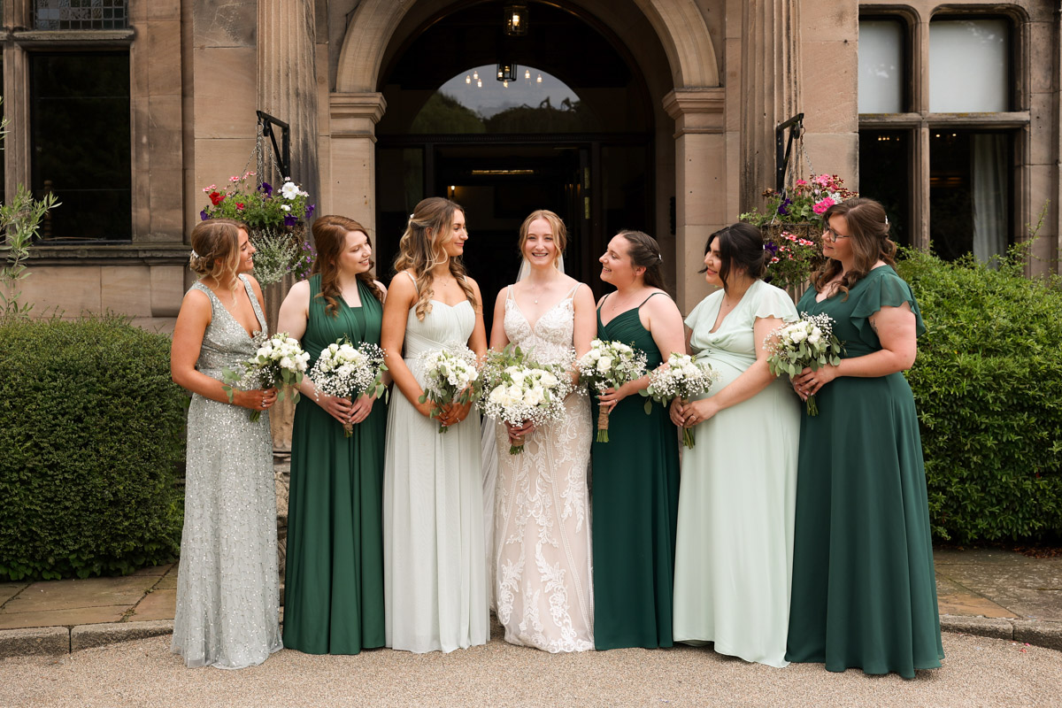 The bride standing with her bridesmaids holding bouquets outside the entrance of Rookery Hall.