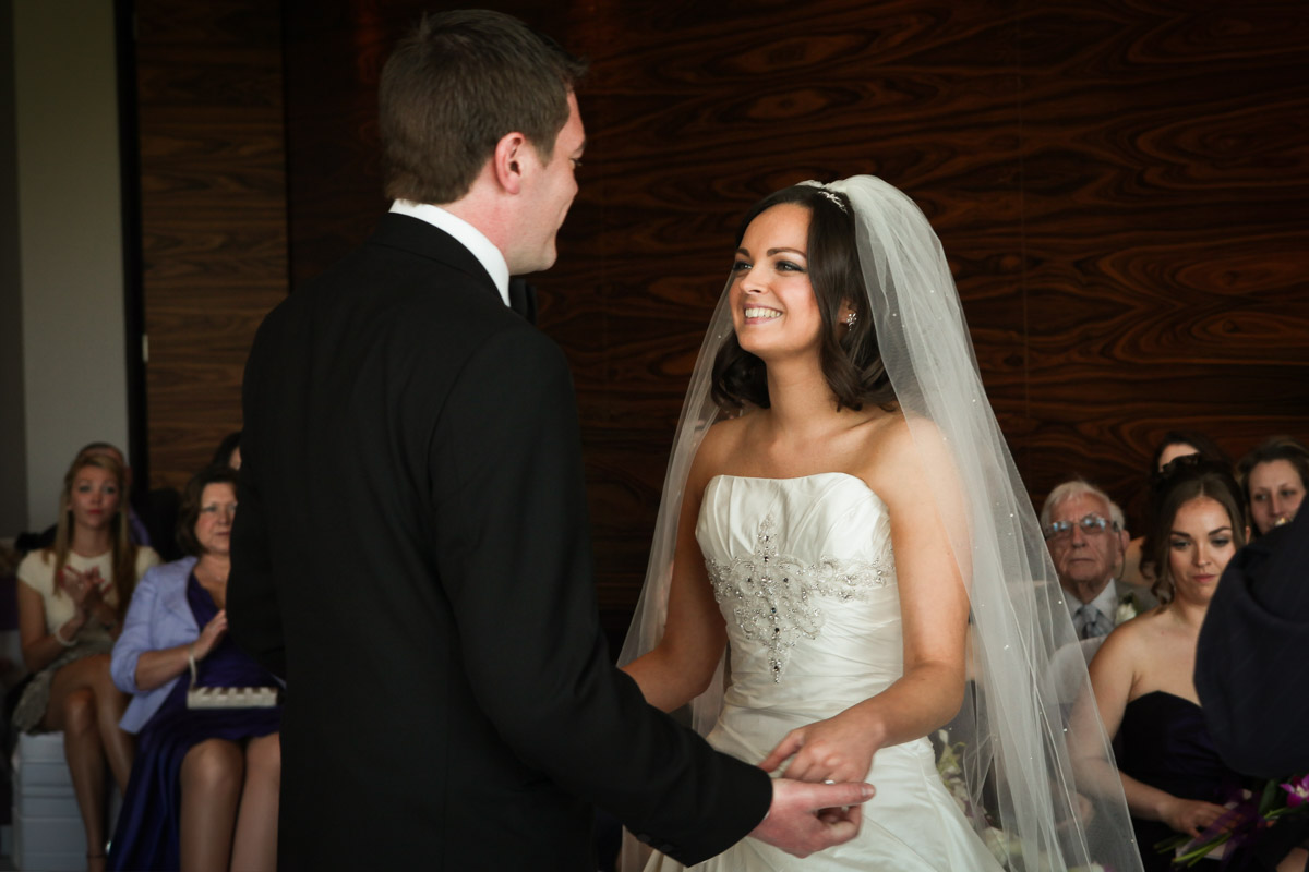Bride and groom smiling and holding hands during a wedding ceremony in the ceremony room at Rookery Hall.