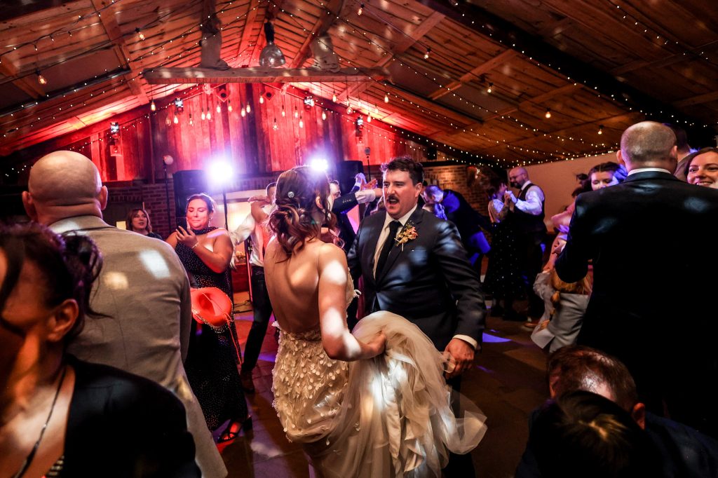 A colorful and lively wedding party enjoying the dancefloor in the main barn at Owen House Wedding Barn