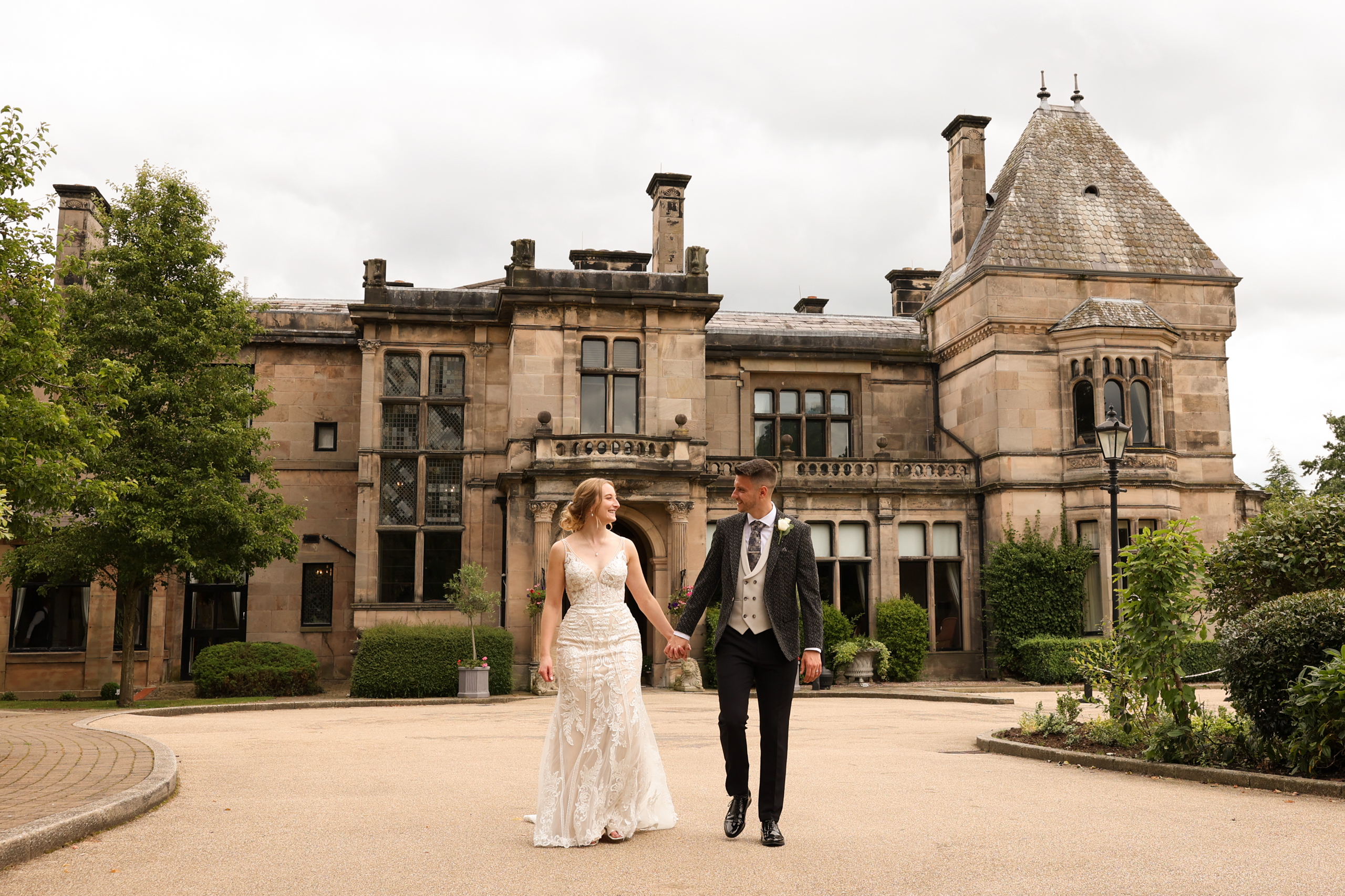 Bride and groom walking hand in hand outside the main entrance of Rookery Hall.