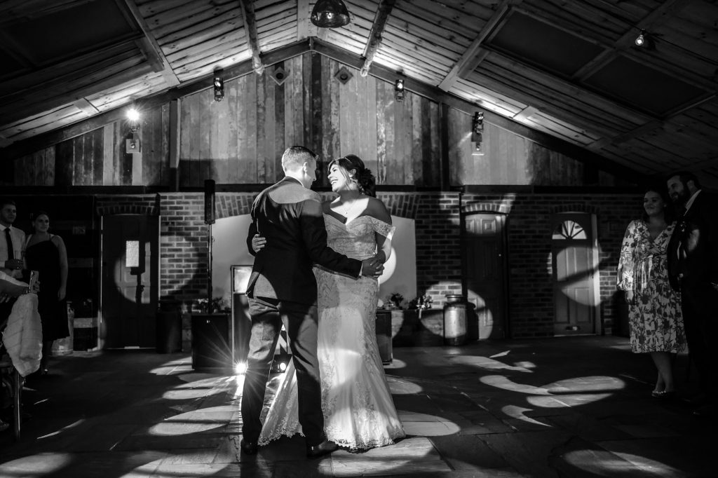 A dramatic black and white wide shot of the first dance under vibrant spotlights at Owen House Wedding Barn