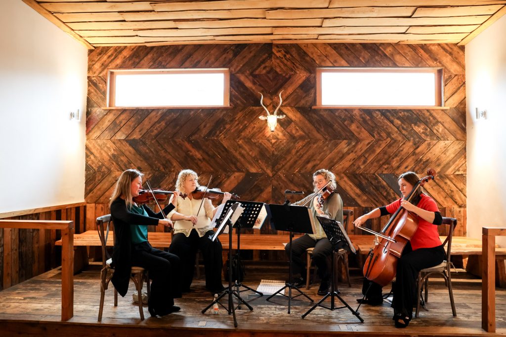 An elegant string quartet performing during a wedding ceremony in the main ceremony barn at Owen House Wedding Barn