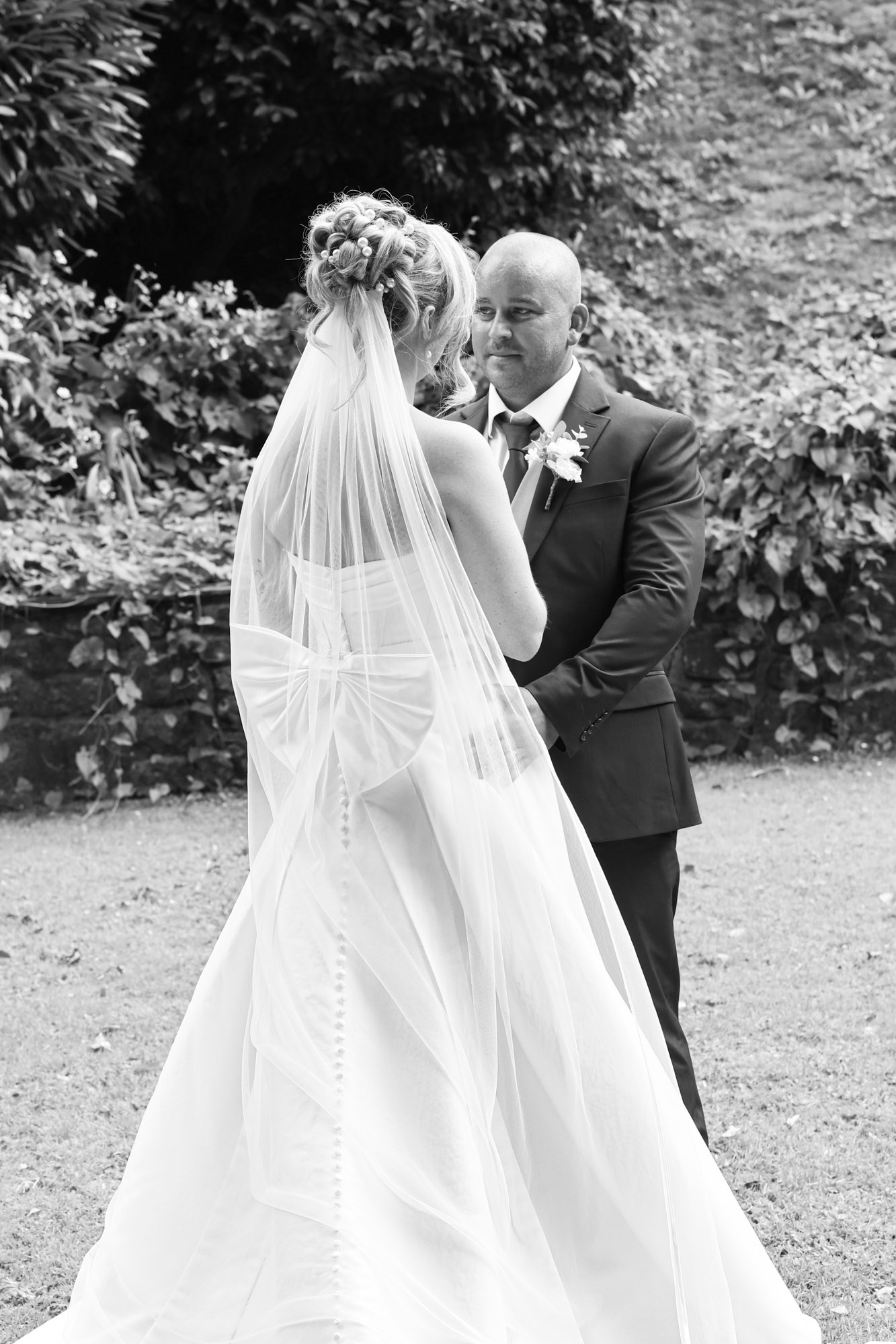 Black and white photo of the bride and groom standing close together outdoors with lush greenery in the background at Mitton Hall.
