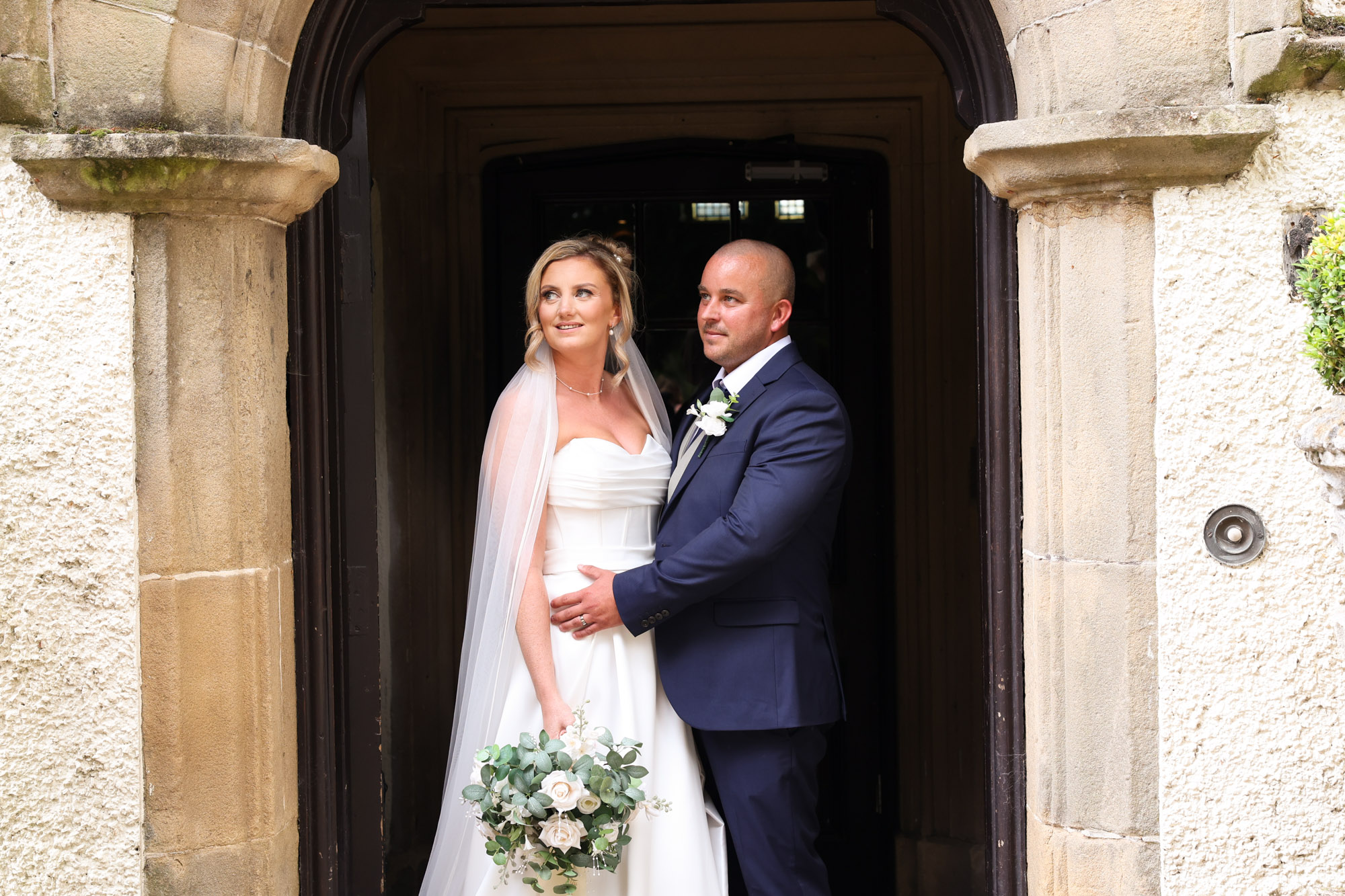 The bride and groom posing together inside the stone doorway entrance at Mitton Hall.