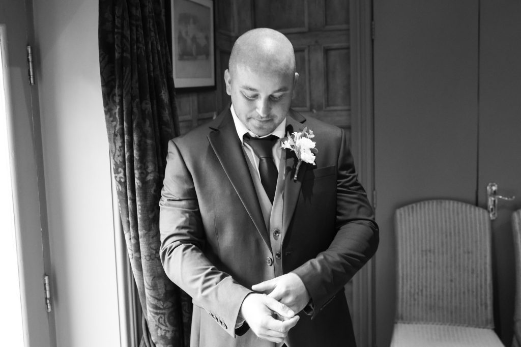 Black and white photo of the groom adjusting his cuffs during preparations at Mitton Hall.
