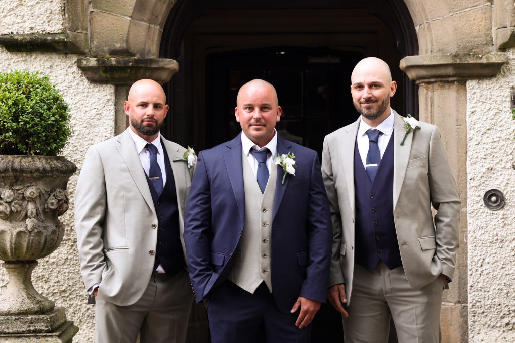 The groom and groomsmen posing together outside the entrance at Mitton Hall.