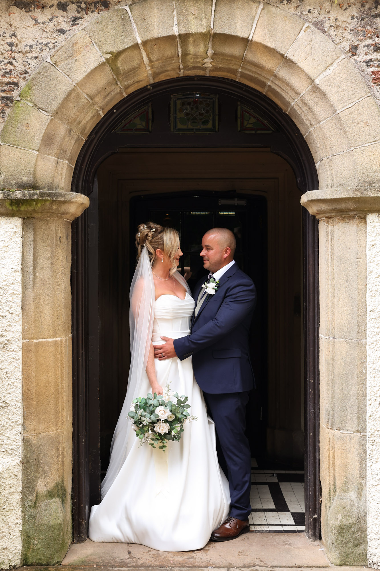 The bride and groom posing together within a stone archway entrance at Mitton Hall.