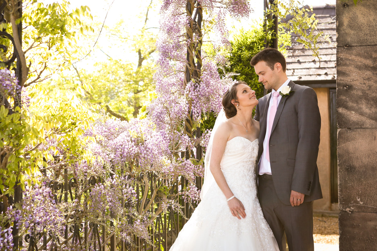 Bride and groom gazing at each other next to blooming wisteria at Rookery Hall.