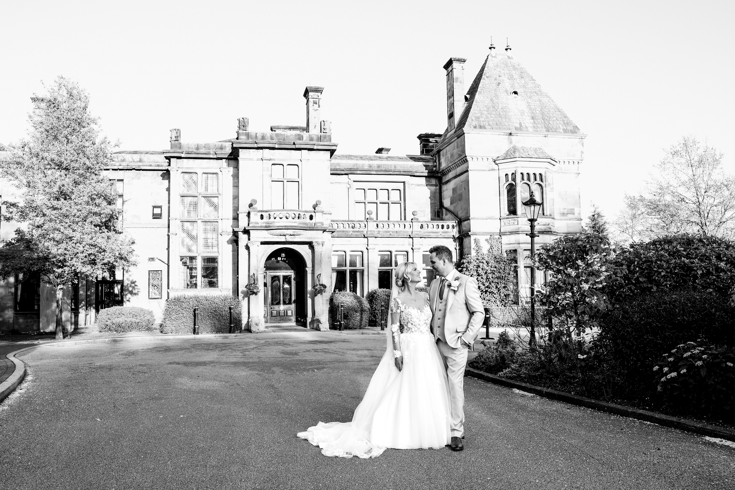 Black-and-white editorial wedding portrait of a bride and groom outside the grand facade of Rookery Hall.
