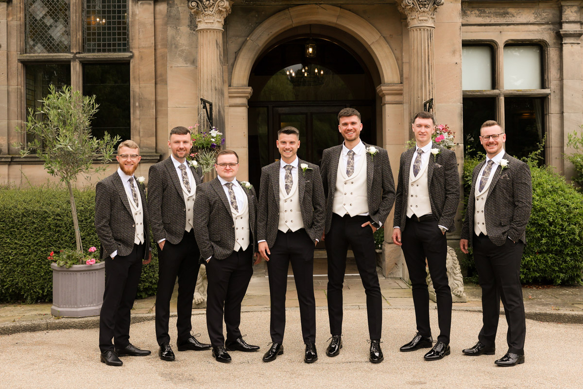 Groom and groomsmen posing in matching suits outside the entrance of Rookery Hall.