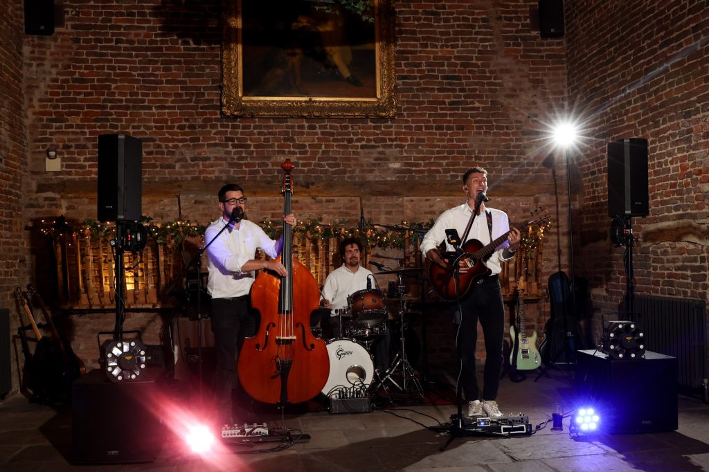 Three-piece band playing live music in a rustic brick room with stage lighting.