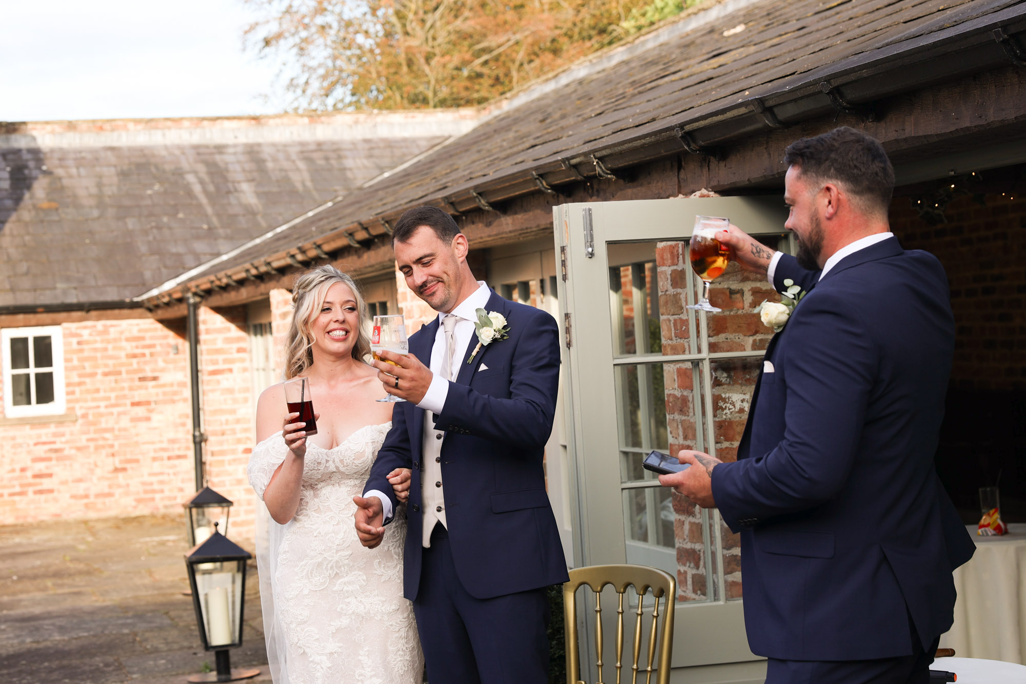 Bride and groom smiling and raising glasses during a wedding toast outdoors.