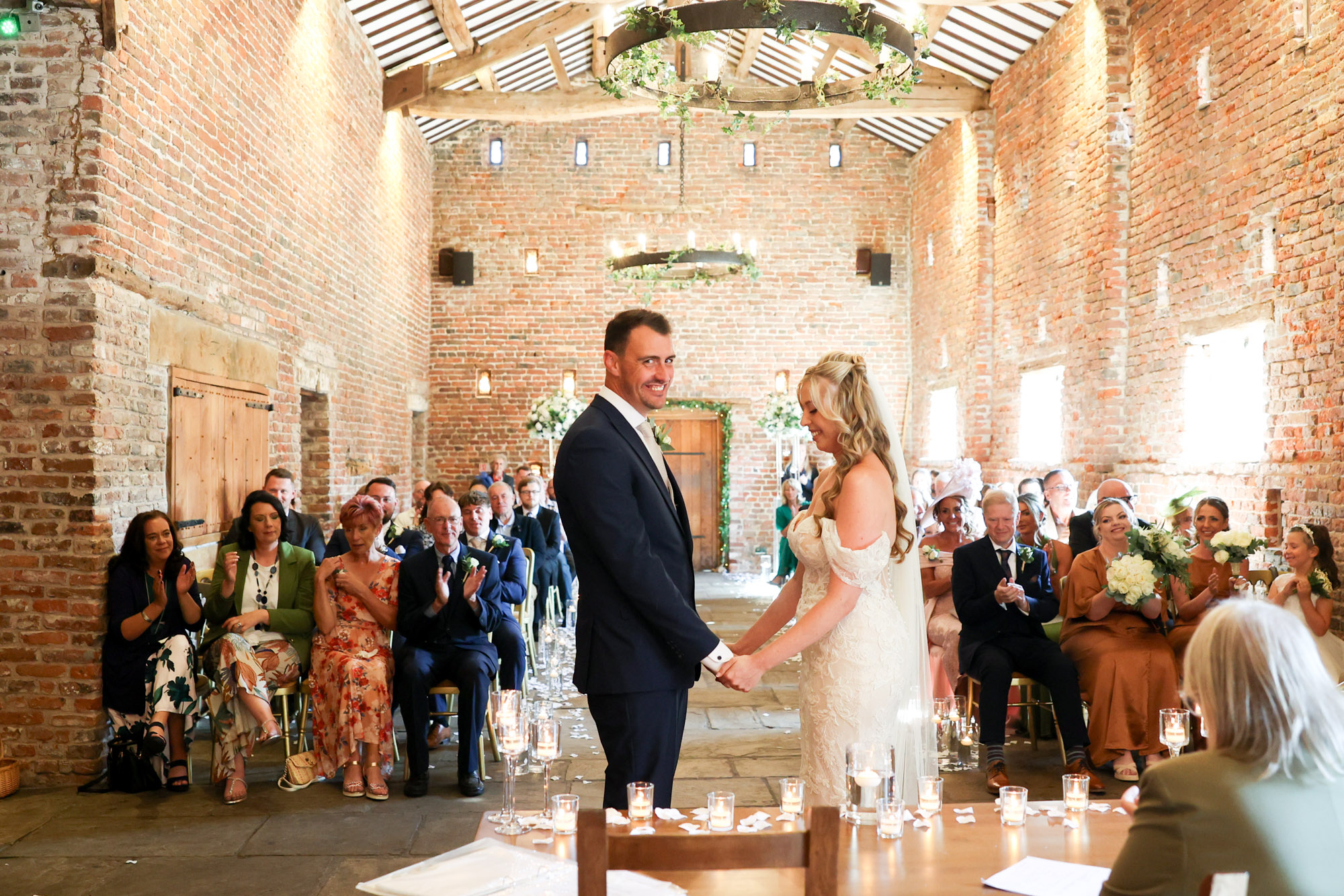 Bride and groom smiling and holding hands at the altar during their wedding ceremony in a rustic brick barn.