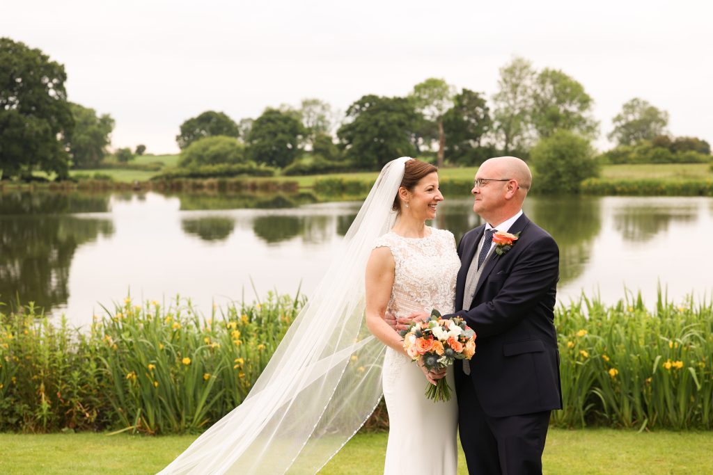 Bride and groom posing together by a tranquil lake at Sandhole Oak Barn.