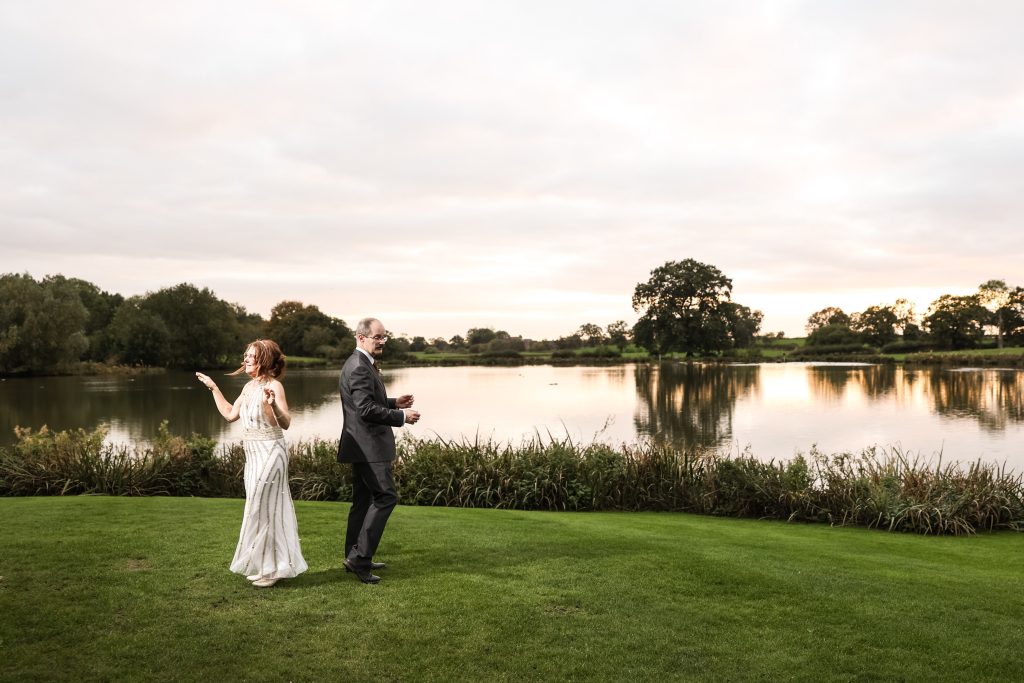 Couple dancing outdoors on the lawn near the lake at sunset.