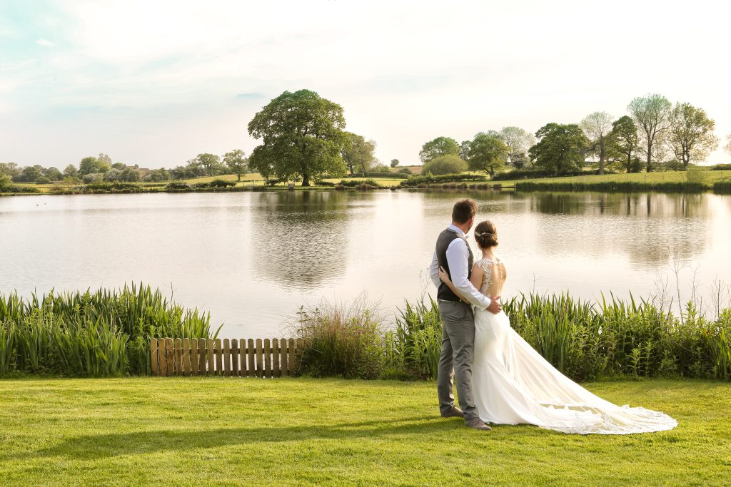 Bride and groom looking out over the scenic lake and countryside at Sandhole Oak Barn.