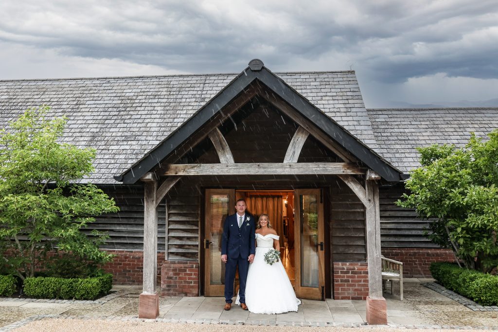 Bride and groom smiling under the doorway porch of Sandhole Oak Barn during a rain shower.