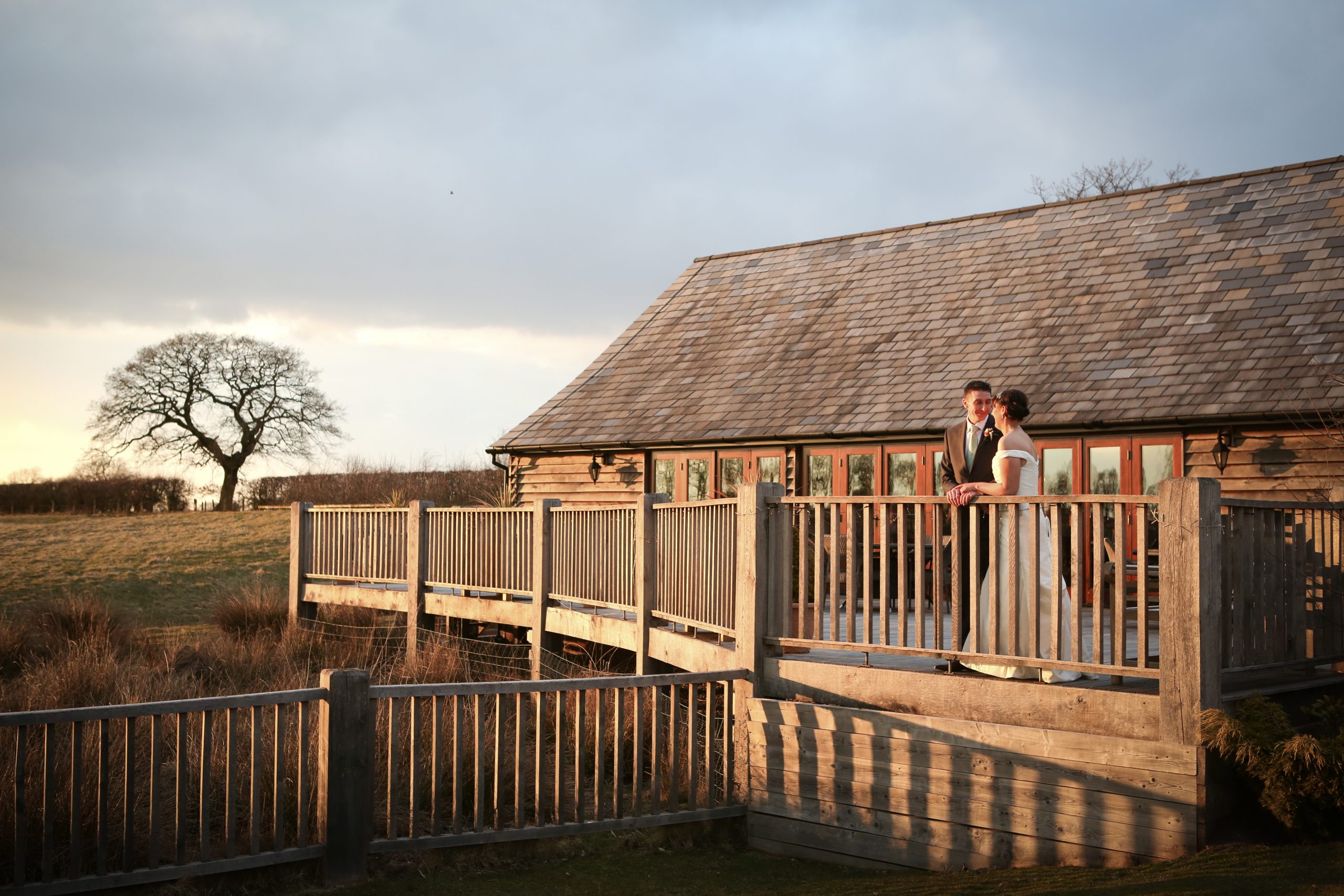 Bride and groom standing together on a wooden barn balcony at golden hour.