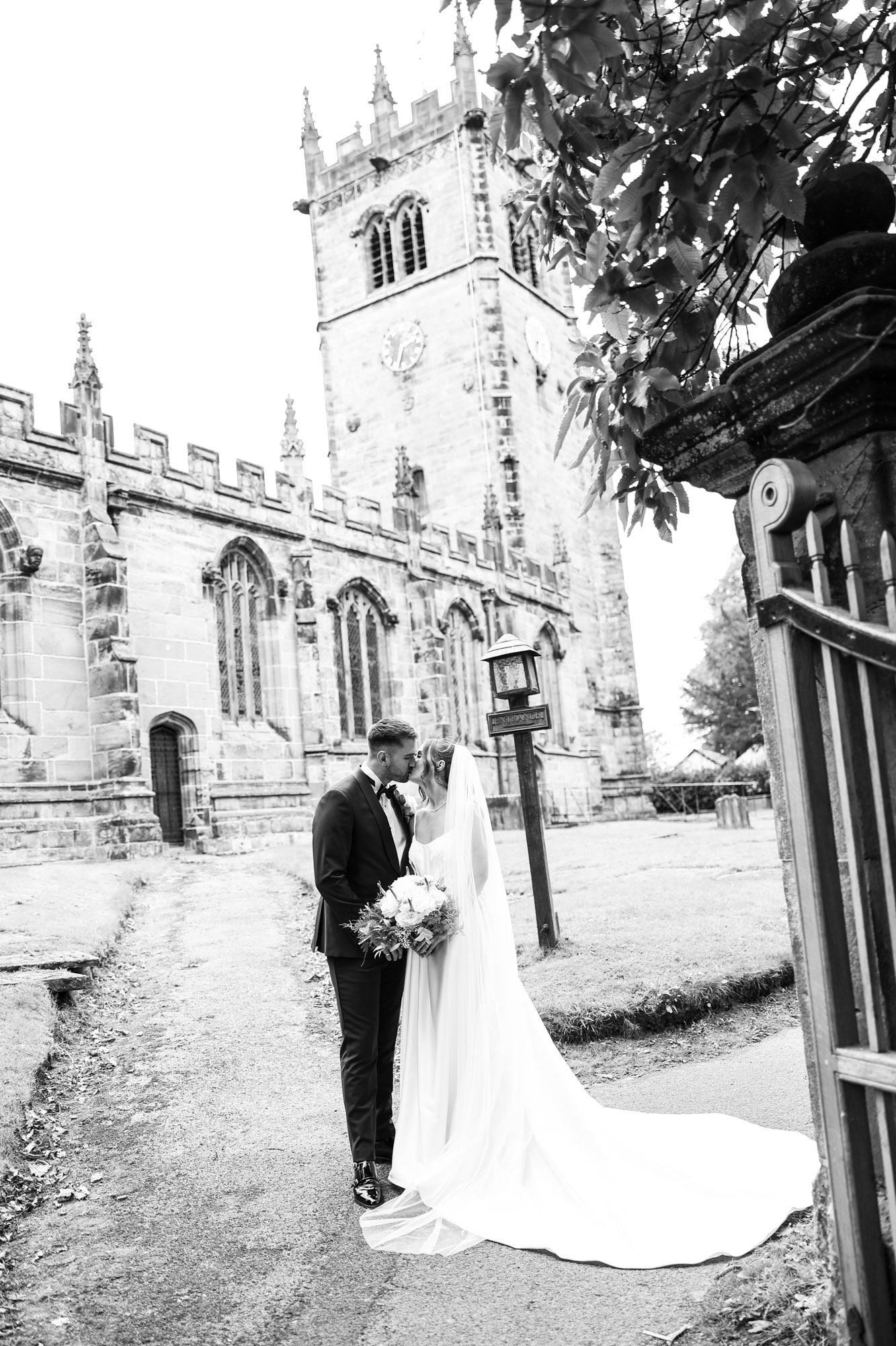 Black and white photo of bride and groom kissing outside historical stone church.