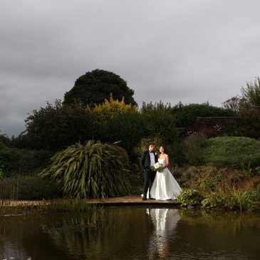 Bride and groom posing in front of a garden pond and dense shrubbery.