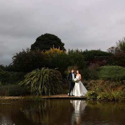 Bride and groom posing in front of a garden pond and dense shrubbery.