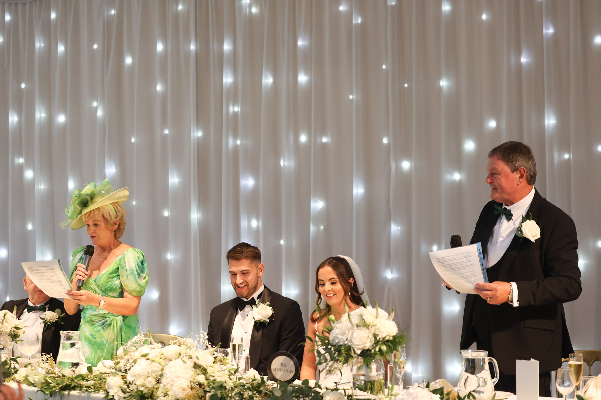 Wedding speeches at the top table with family members speaking while the bride and groom listen.